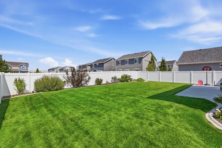 Expansive backyard featuring a manicured lawn, established landscaping, white privacy fencing, and a concrete patio