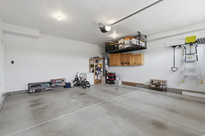 Spacious garage with concrete flooring, overhead storage racks, and warm wood-finish cabinetry