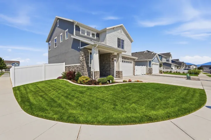 Two-story residence featuring a combination of stucco and siding, stone accents, an attached two-car garage, front yard landscaping, and a surrounding white fence