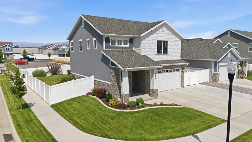 Contemporary two-story residence featuring a combination of siding and stone veneer, a two-car garage, and a landscaped front yard with a white privacy fence