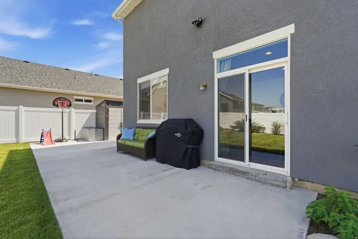 Concrete patio area with a stucco exterior, sliding glass door, and a white vinyl fence