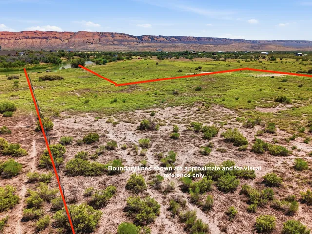 Expansive land parcel featuring natural vegetation, a river, and distant red rock formations under a clear sky