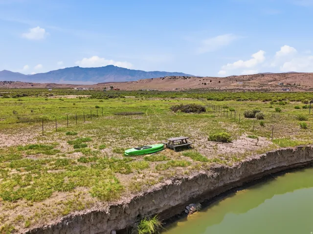 Expansive open terrain with natural vegetation, defined by fencing, and bordered by a water feature