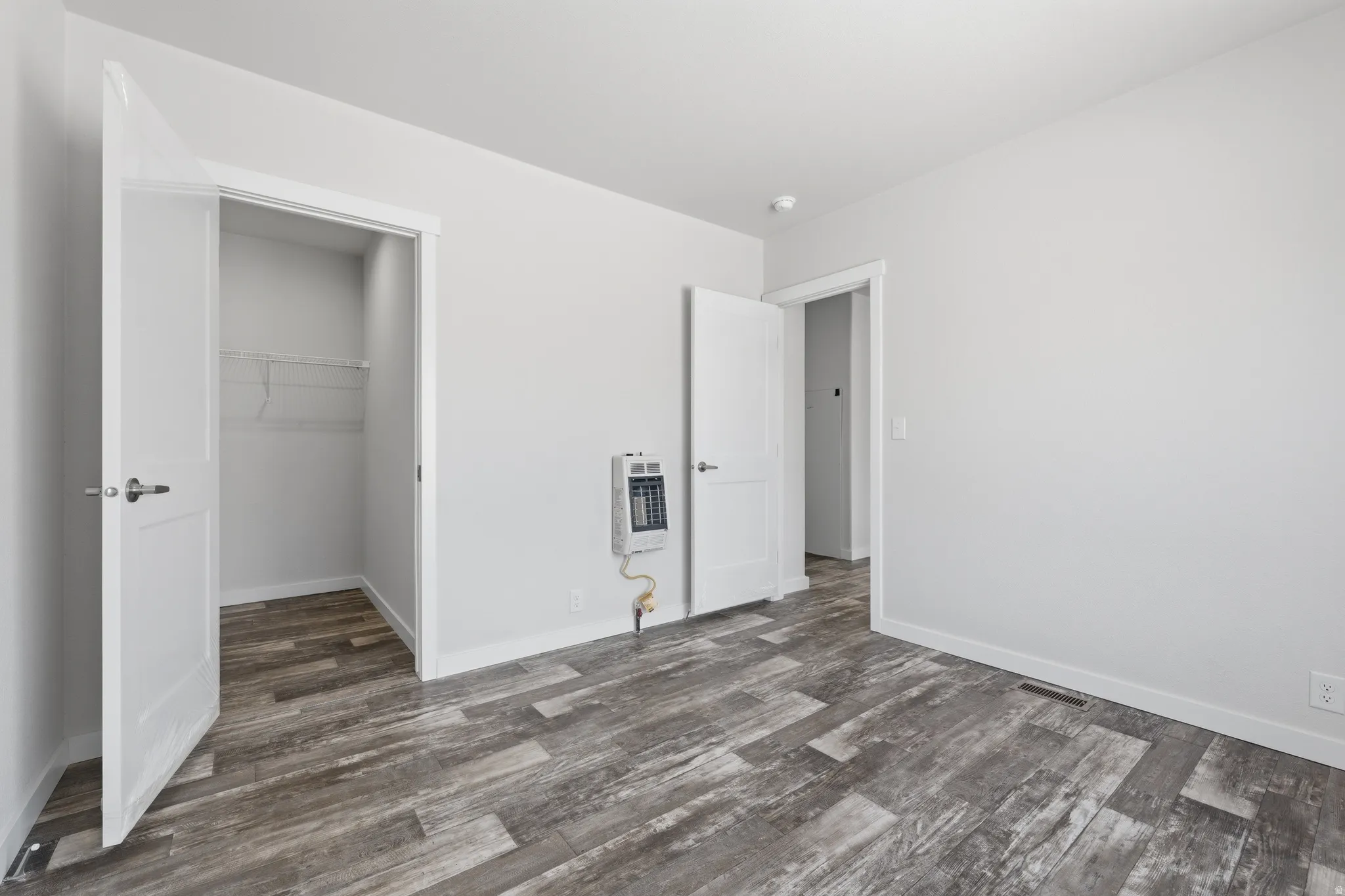 Wood-finish flooring with crisp white baseboards, a built-in wall heater, and a closet with wire shelving
