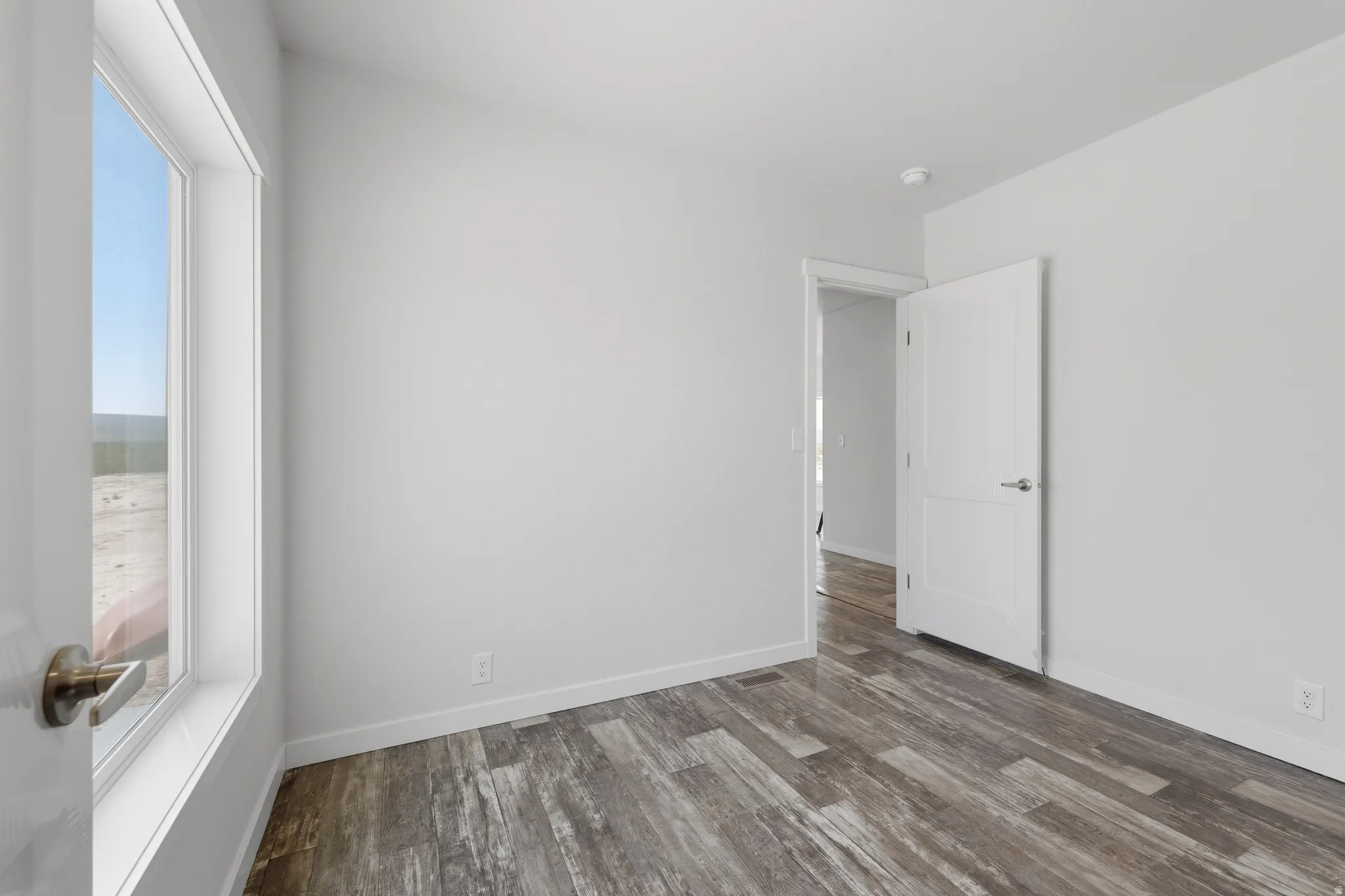 Wood-finish flooring with white baseboards, bright white walls, and a white interior door with a brushed nickel handle