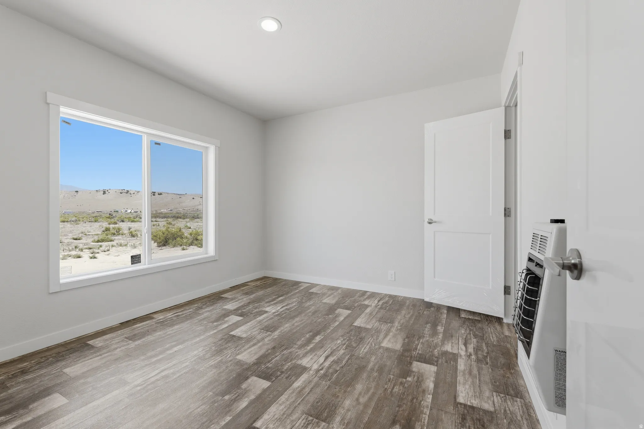 Recessed ceiling lighting, wood-finish flooring, white trim around windows, white interior doors, and a wall-mounted heater
