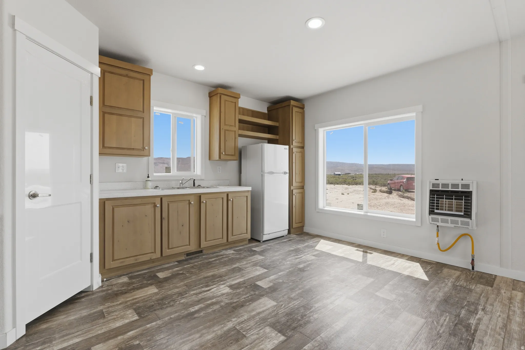 Wood-finish flooring, recessed lighting, double-basin sink, light wood cabinetry, and a wall-mounted heater