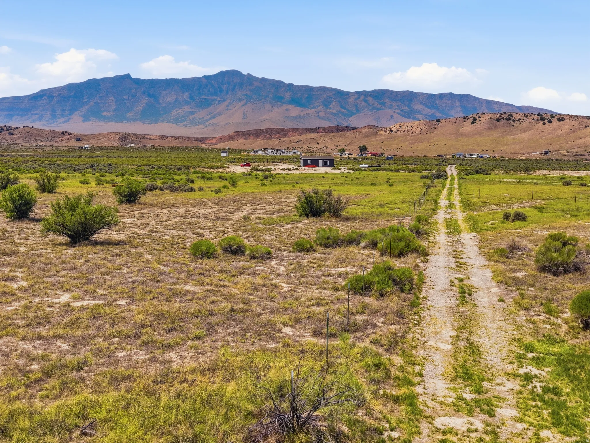 Expansive desert landscape featuring a long unpaved access road, scattered low-lying vegetation, and distant mountain scenery