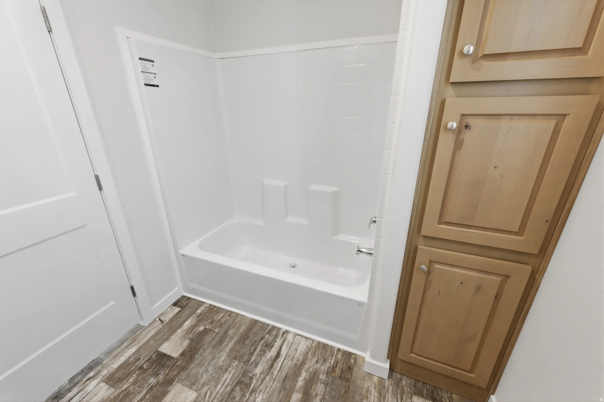 Walk-in shower with a built-in tub, wood-finish flooring, and light wood cabinetry with brushed nickel hardware