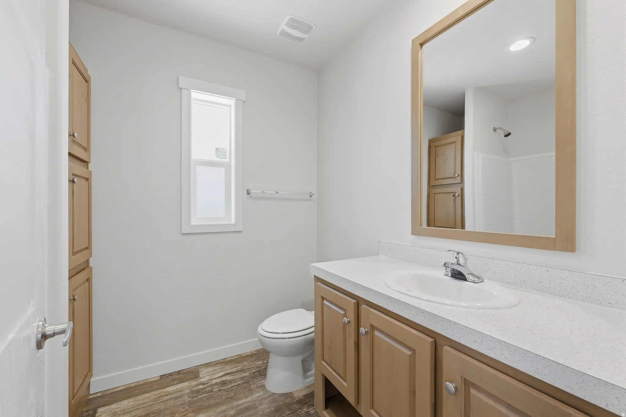 Wood-finish flooring, light-toned wood cabinetry, built-in storage, vanity with integrated sink, and a framed mirror
