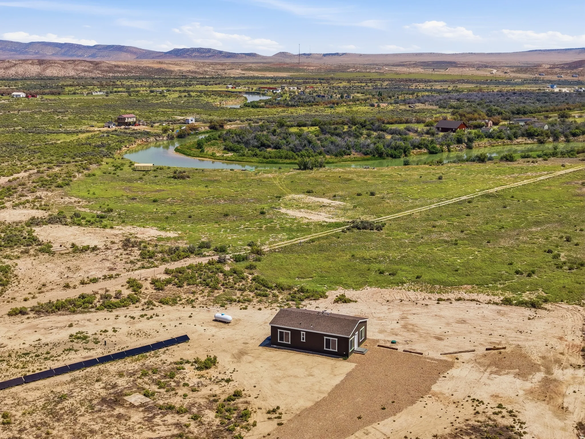 Expansive natural landscape with a winding waterway, featuring a single-story dwelling, solar panel array, and a gravel driveway