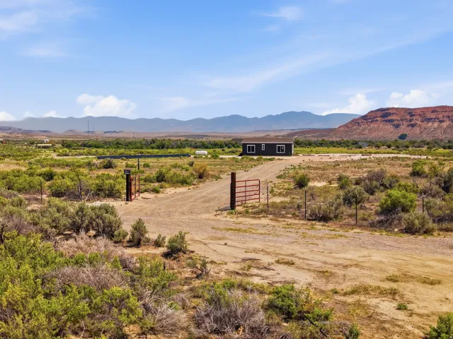 Expansive land with a dark-colored exterior structure, featuring a metal gate entrance and distant mountain formations