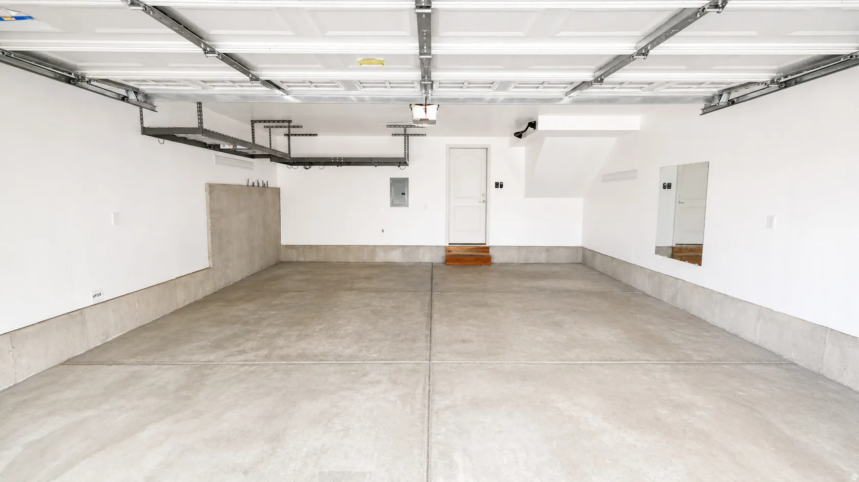 Spacious garage featuring a concrete floor, white painted walls, overhead storage racks, and a panel garage door