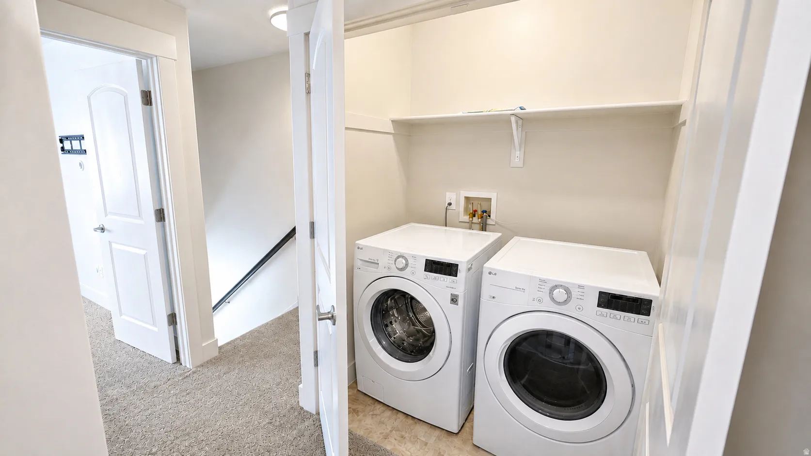 Laundry area with white front-load washer and dryer, built-in shelving, and light-toned flooring