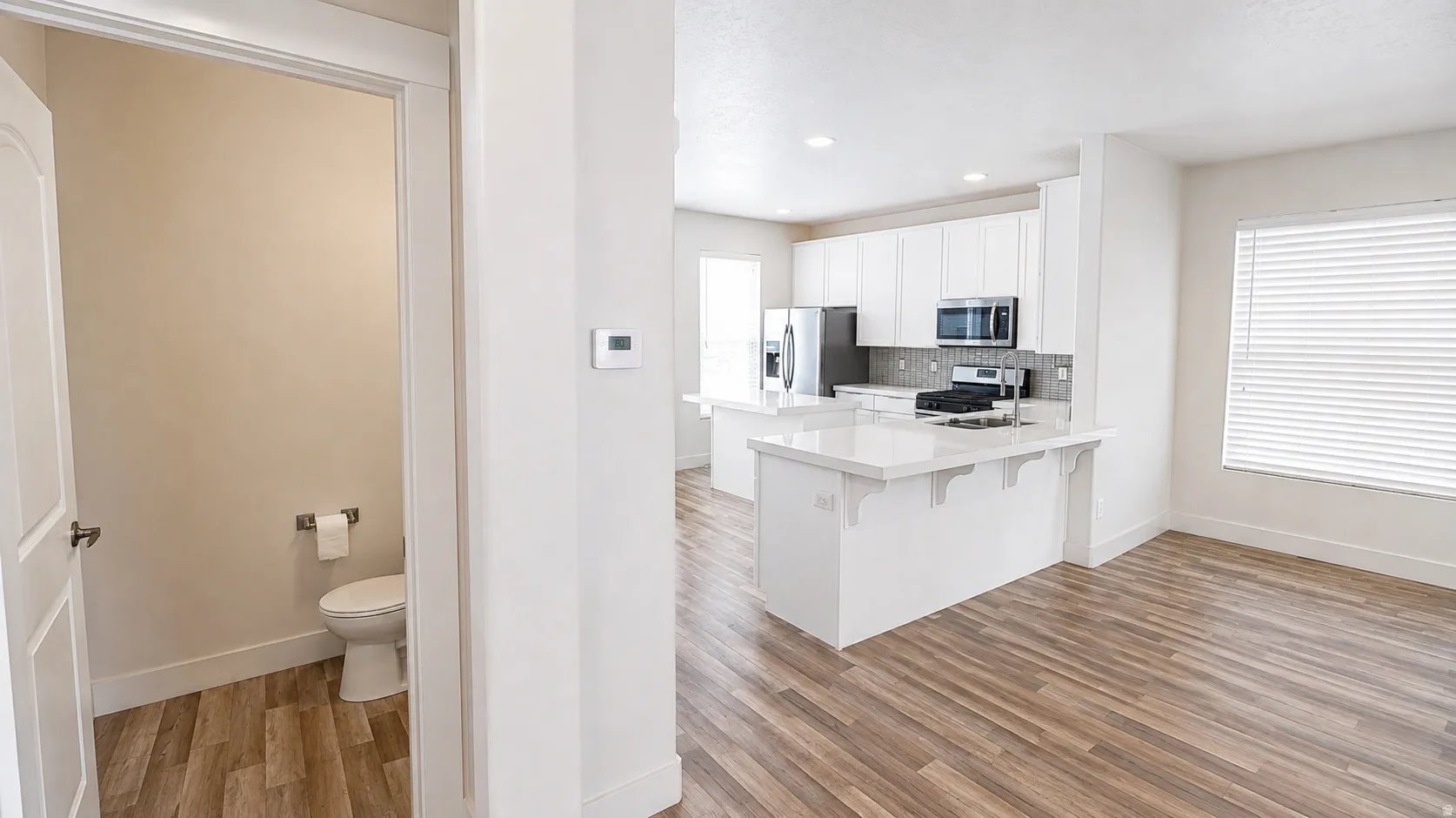 Open-concept layout featuring wood-finish flooring, white cabinetry, integrated appliances, and a kitchen island with seating