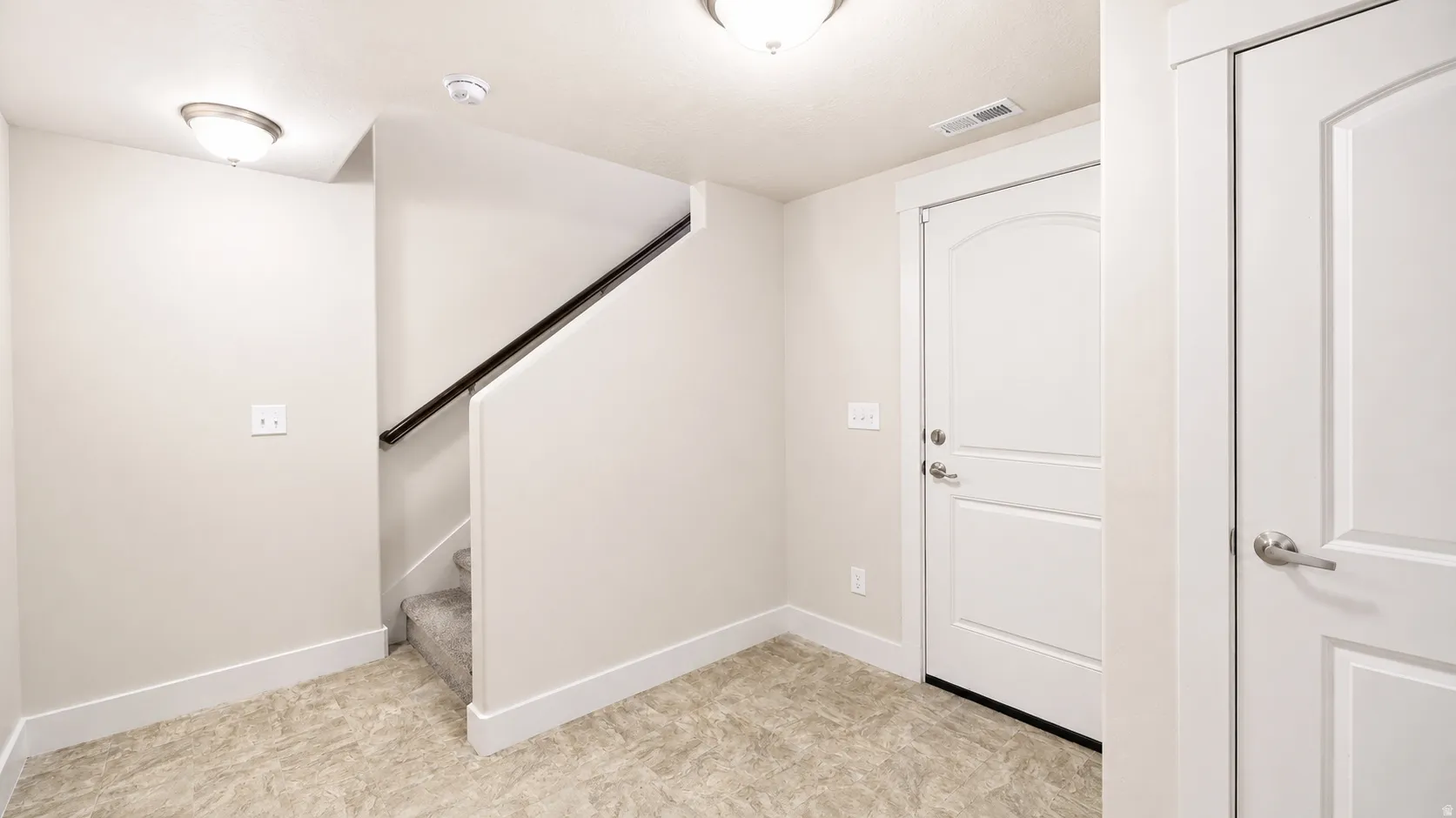 Carpeted staircase with dark wood railing, white paneled doors, and light-toned flooring