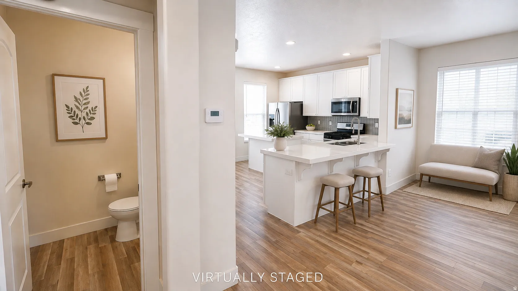 Open-concept living area with wood-finish flooring, a white kitchen island, white cabinetry, and stainless steel appliances