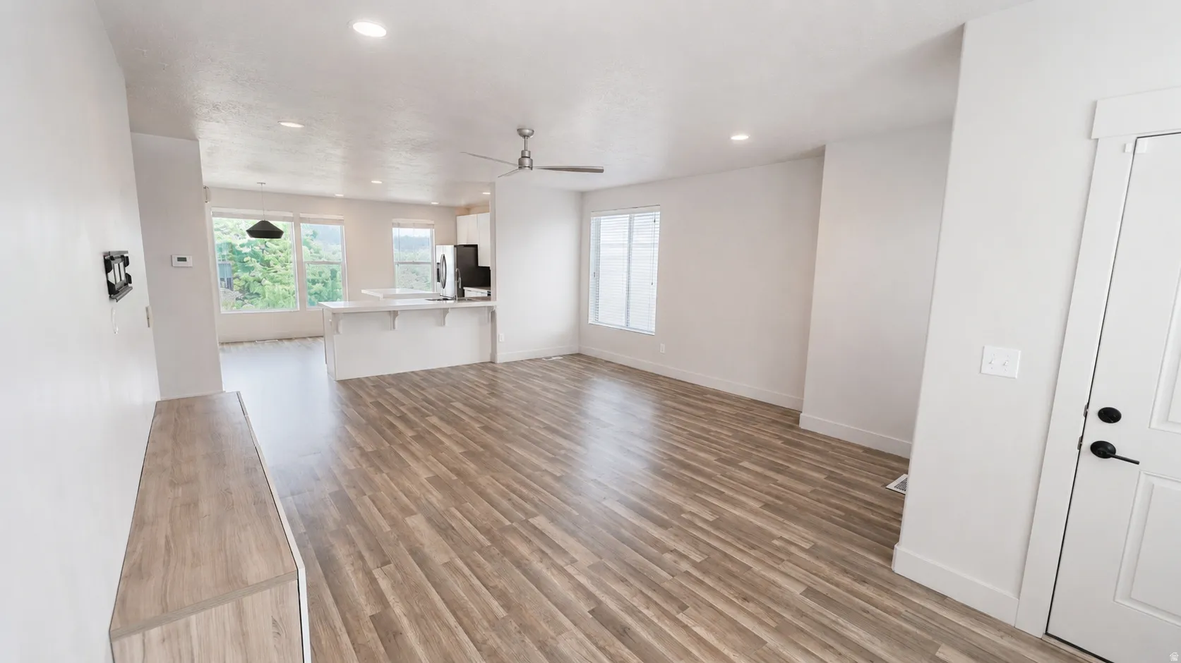 Open-concept living space with wood-finish flooring, recessed lighting, a modern ceiling fan, and white walls