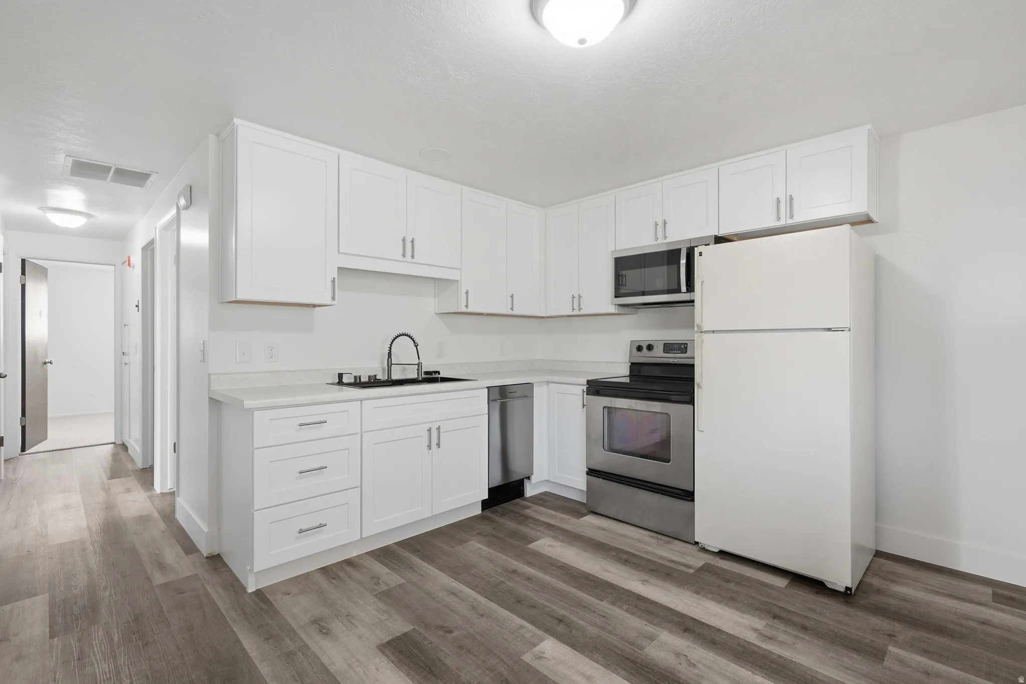 Kitchen featuring white shaker cabinetry, light-toned countertops, stainless steel appliances, and wood-finish flooring