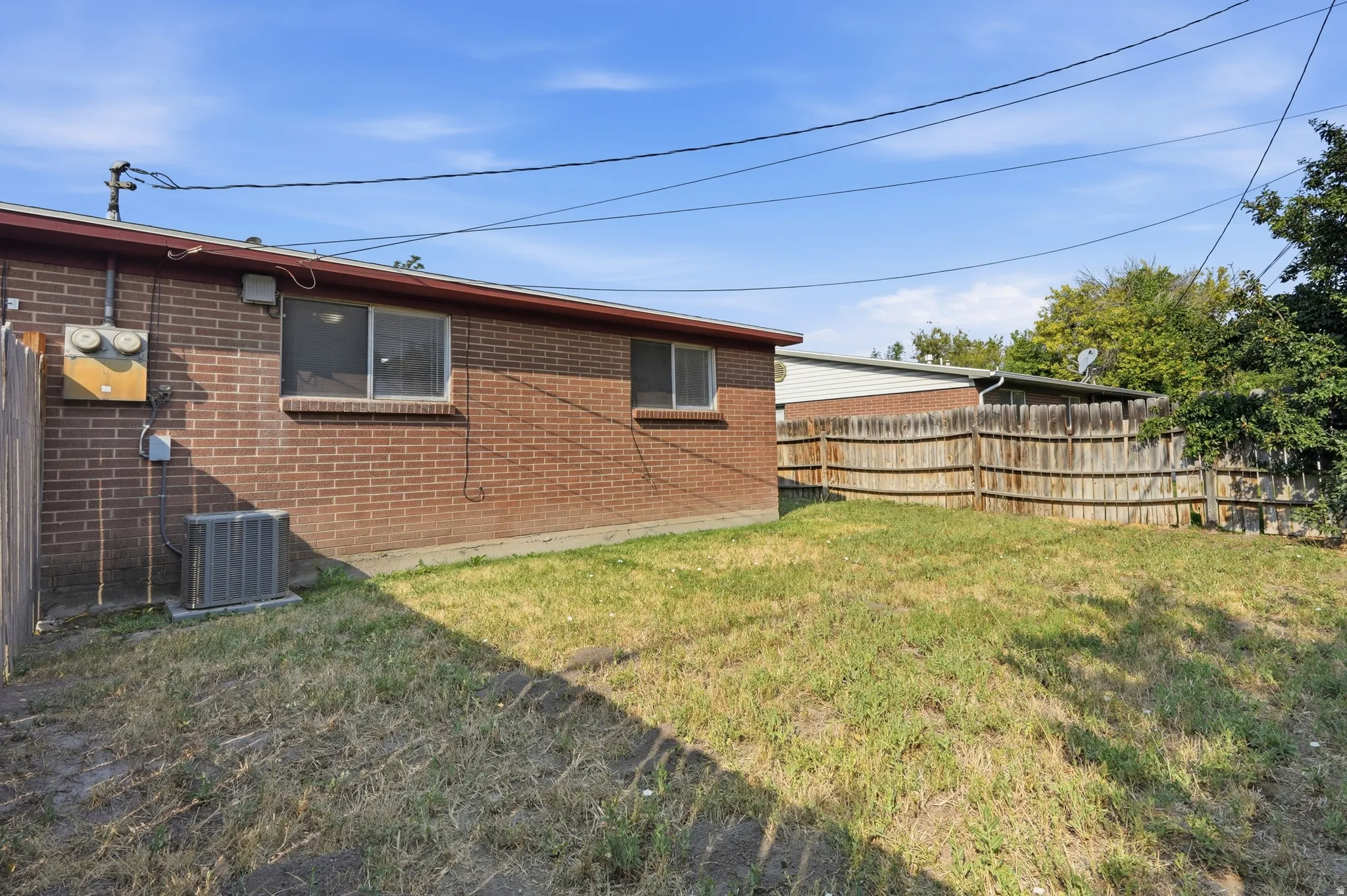 Expansive lawn area with a wood fence, brick exterior, and multiple windows