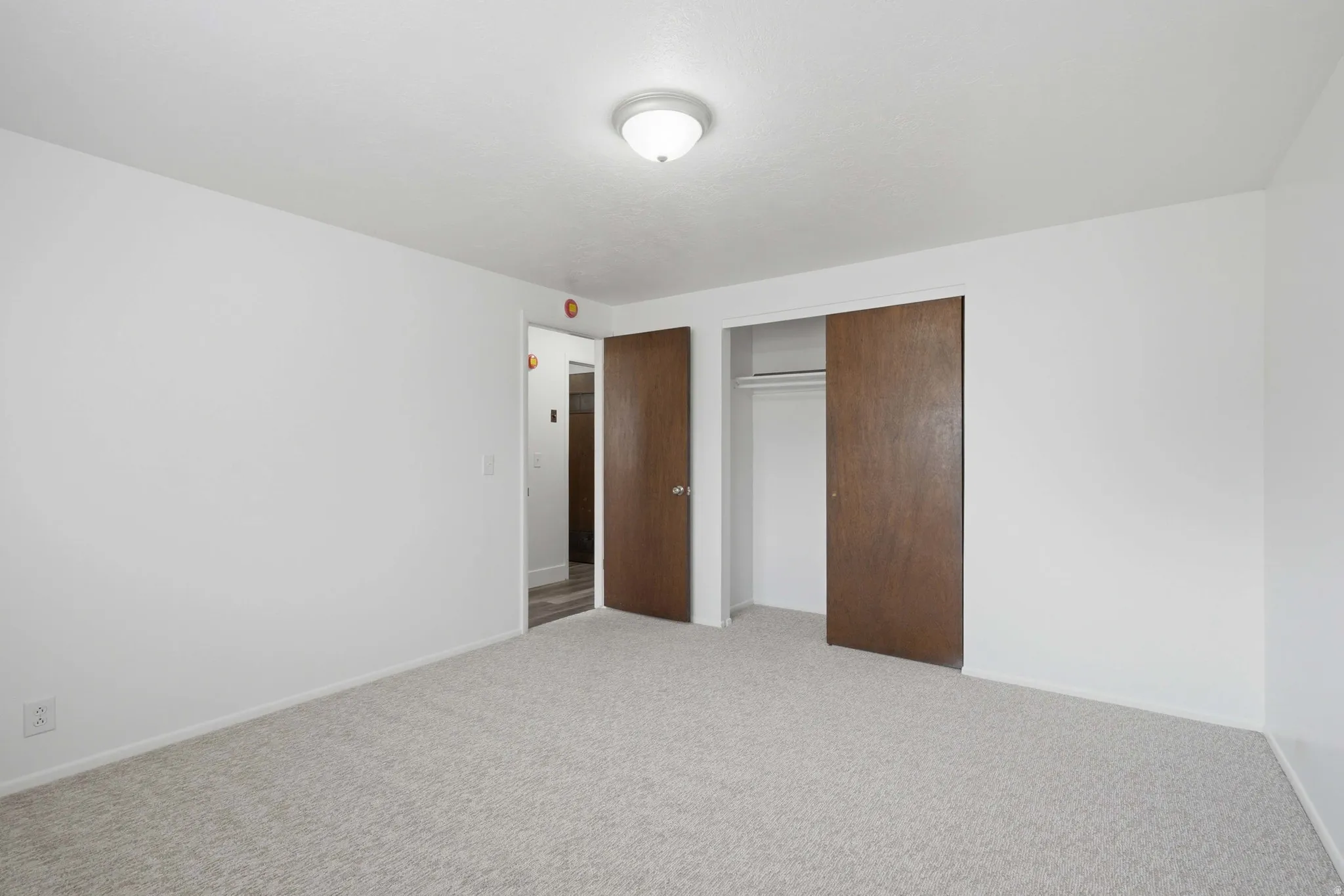 White walls, light-toned carpeting, and a flush mount ceiling light