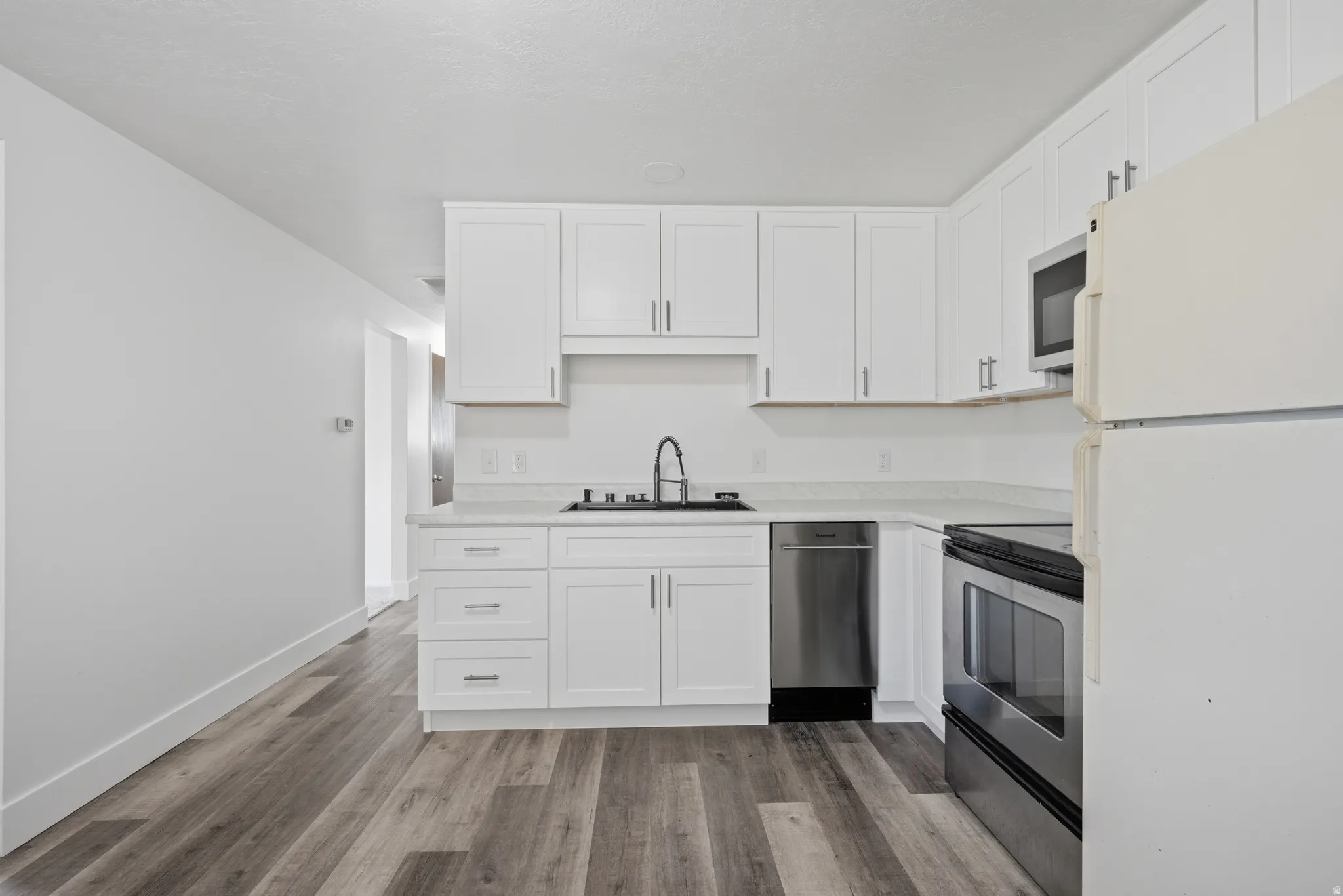 White shaker-style cabinetry with chrome hardware, wood-finish flooring, undermount sink with a matte black faucet, and stainless steel appliances
