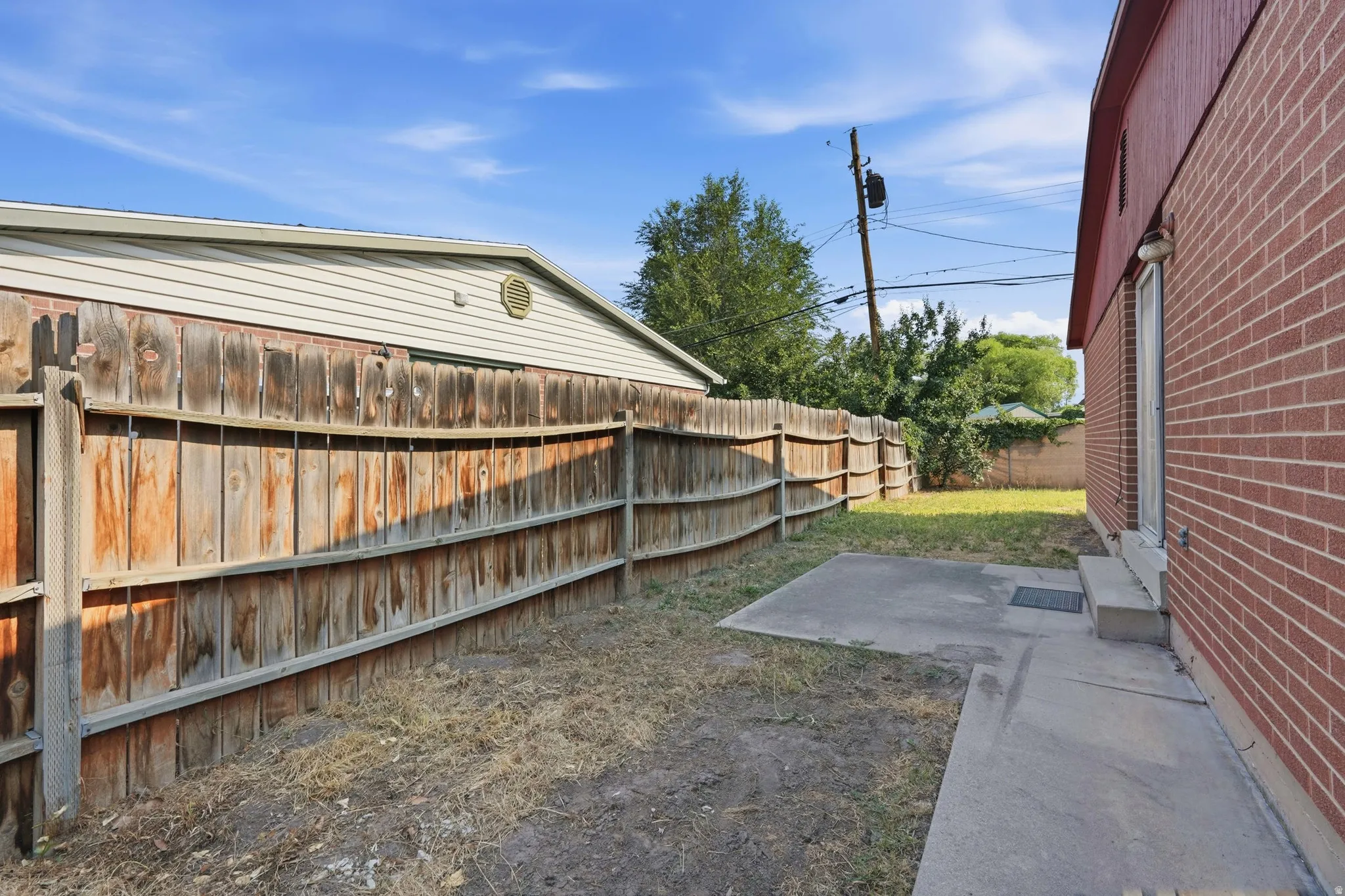 Fenced backyard featuring a concrete patio, brick exterior, and a secondary grass area