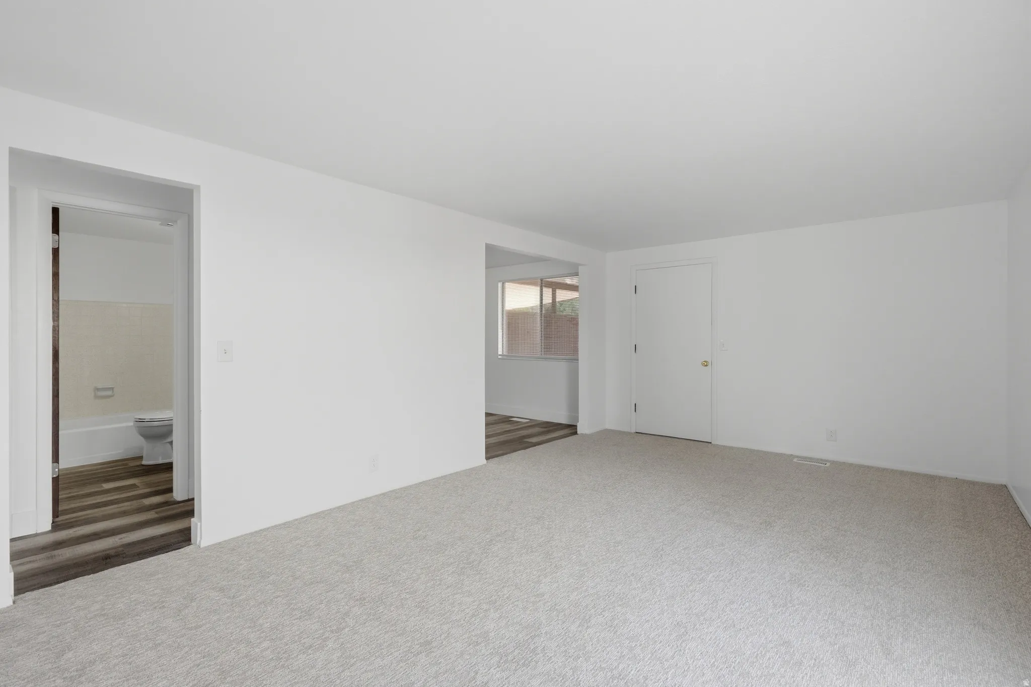 Neutral-toned carpeting, white walls, white interior doors, and wood-finish flooring in adjacent spaces