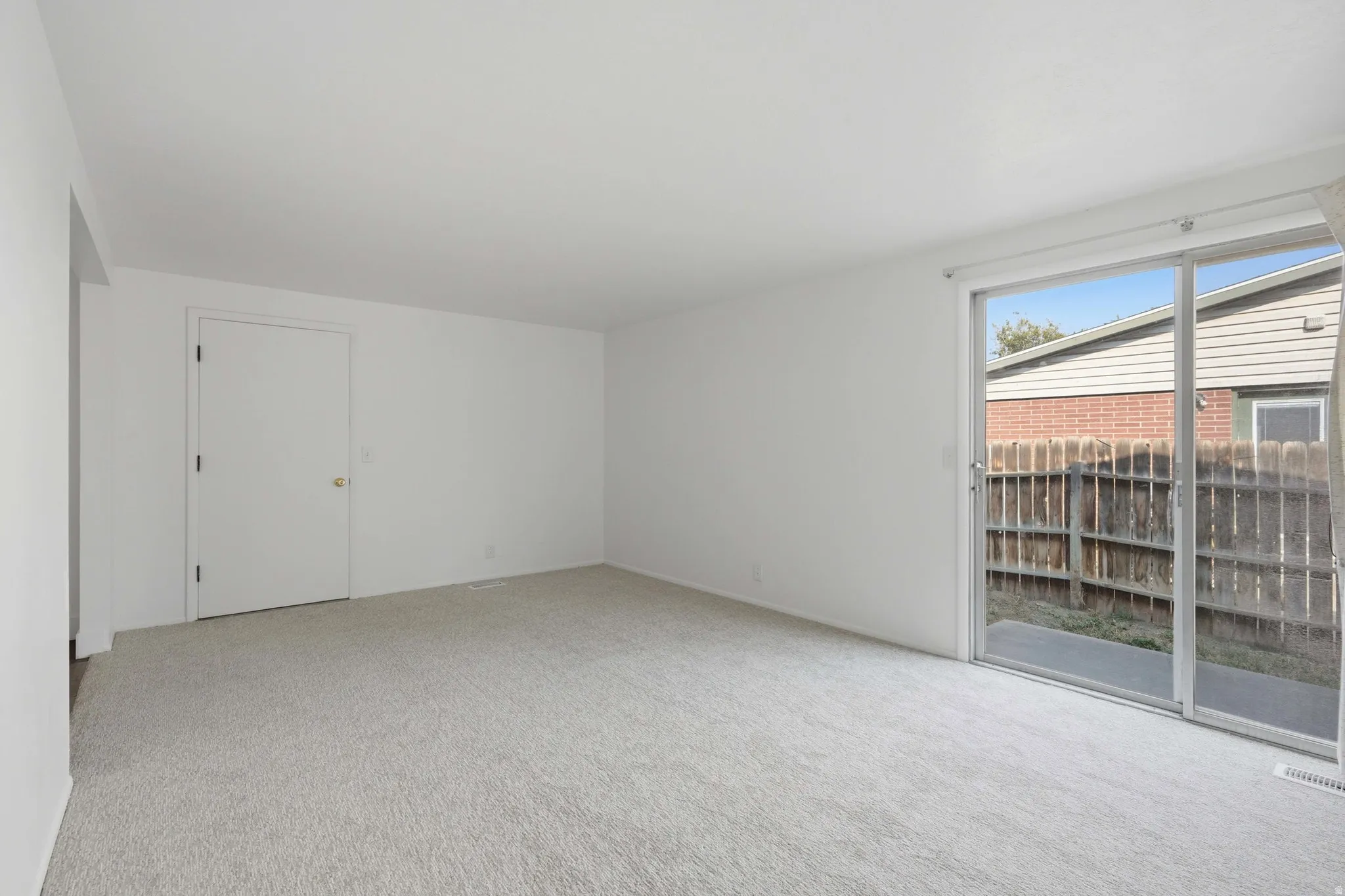 Light gray carpeting, white painted walls, and a sliding glass door to a concrete patio