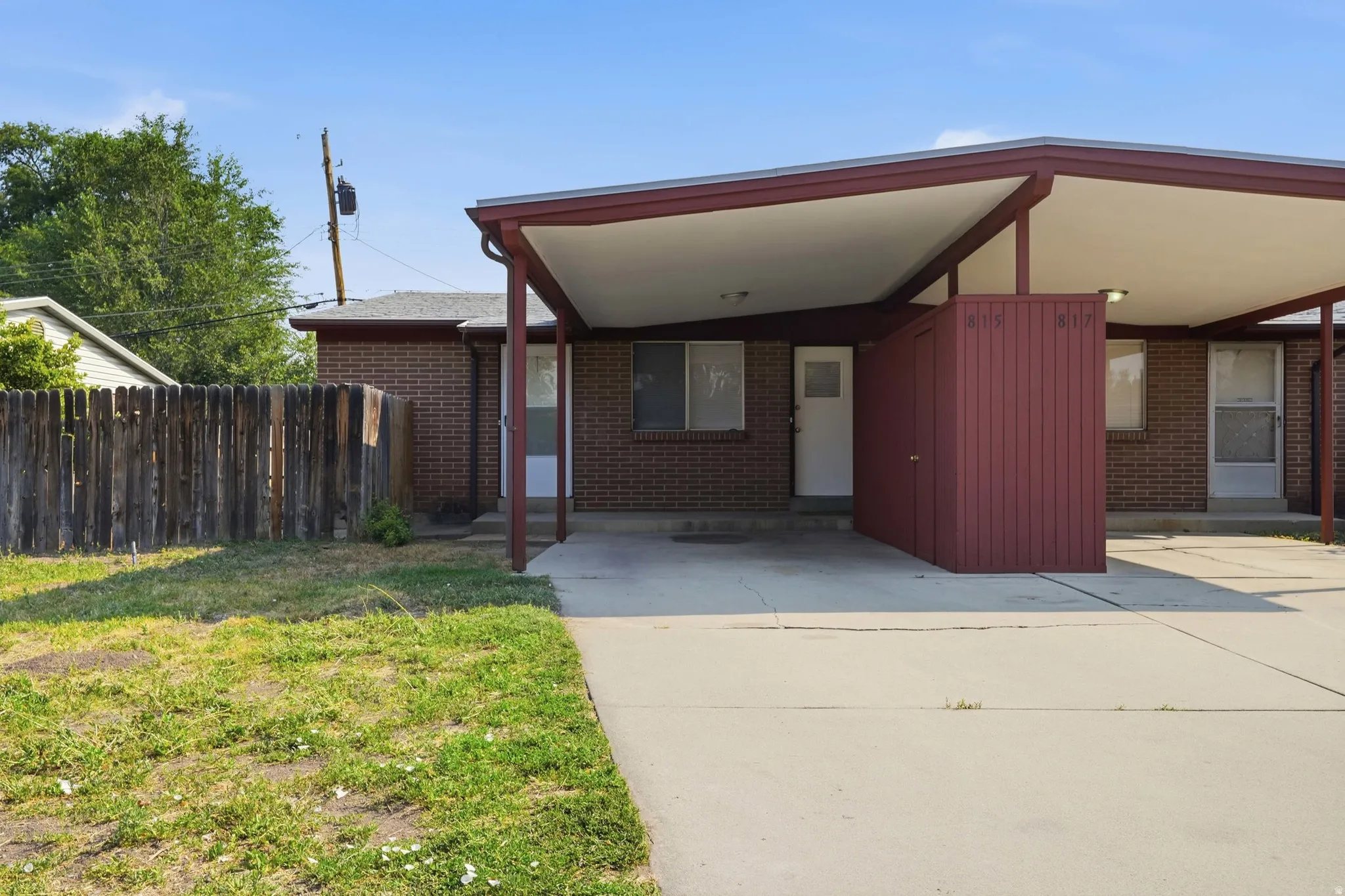 Brick exterior with covered carports, concrete drive, and wood privacy fencing