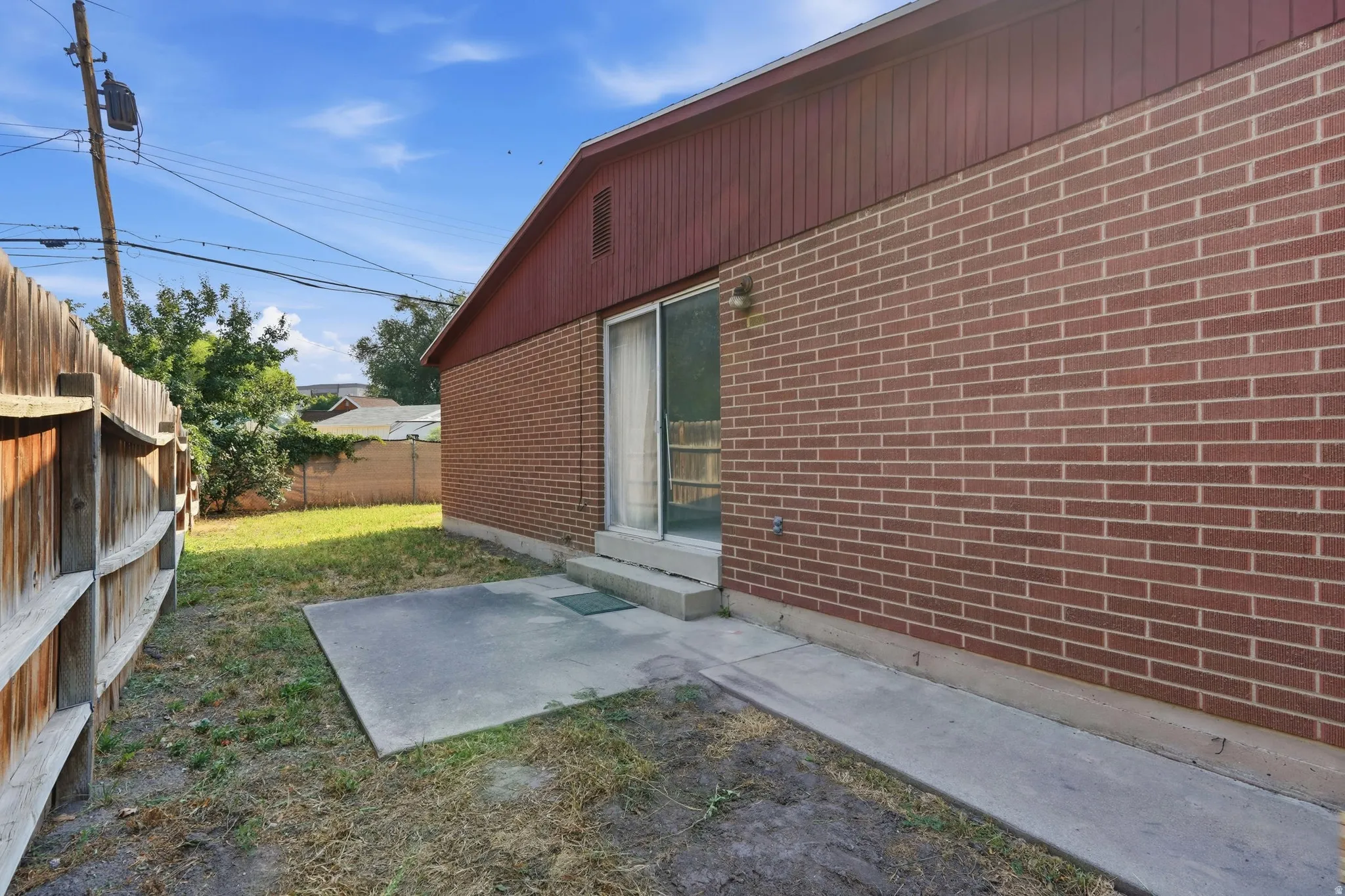 Red brick exterior with a wood fence, concrete patio, and sliding glass door