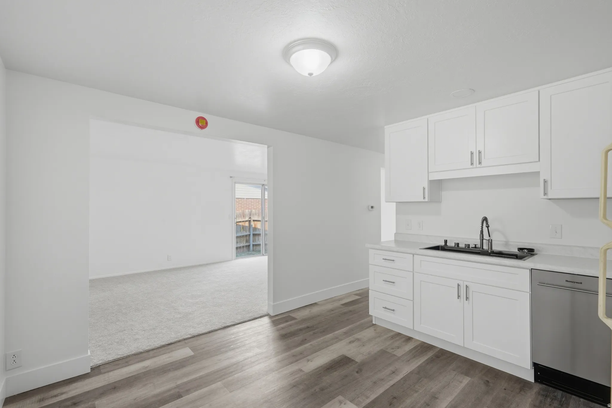 Kitchen featuring wood-finish flooring, white cabinetry, a stainless steel dishwasher, and light-toned countertops