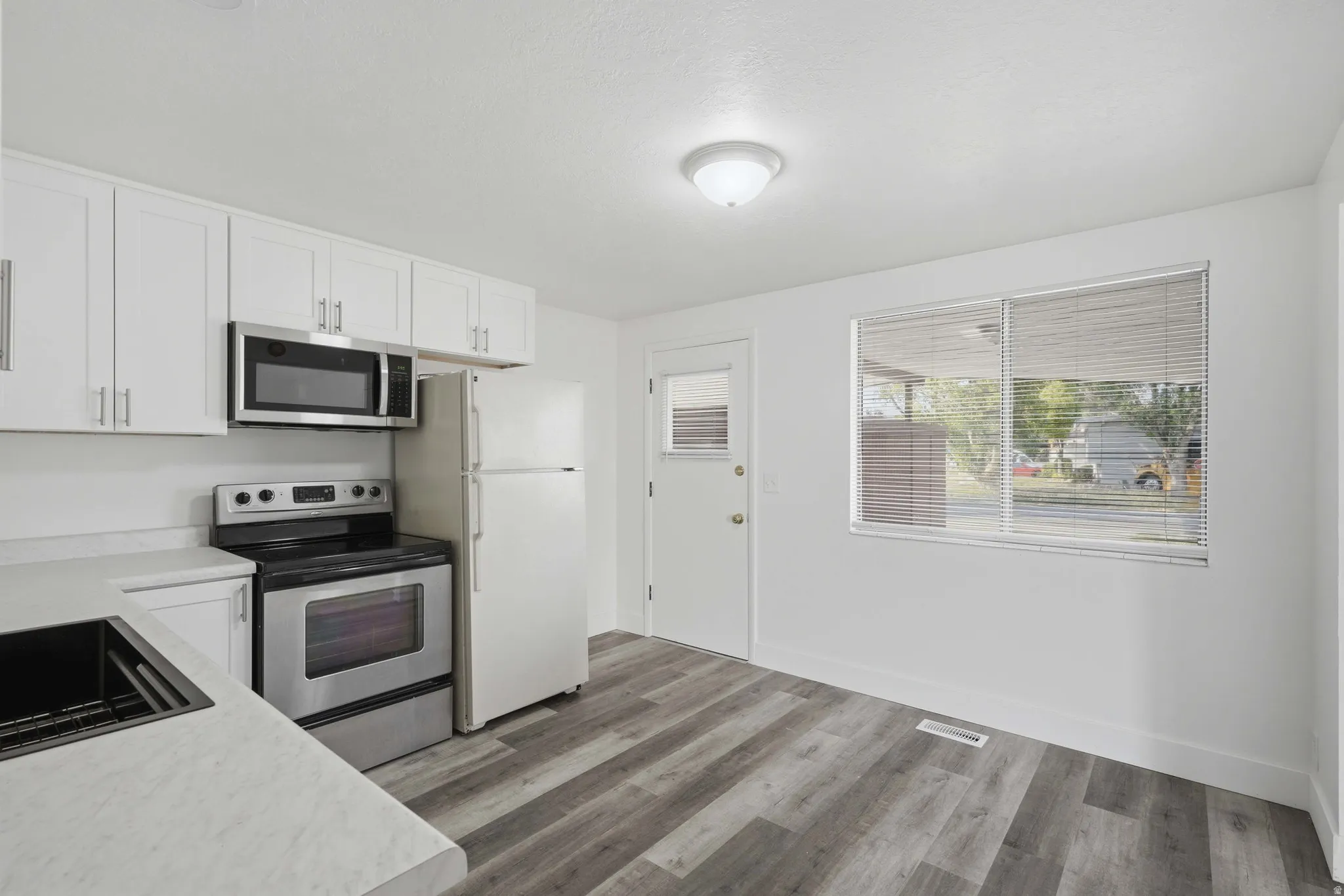 White cabinetry, stainless steel appliances, wood-finish flooring, white countertops, and a flush mount ceiling light