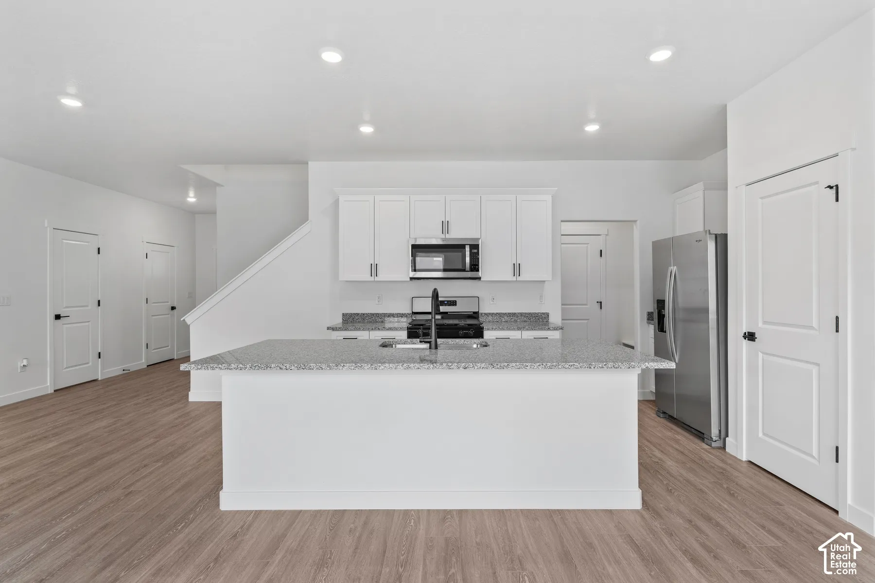 Open-concept kitchen with a central island, white cabinetry, integrated stainless steel appliances, and wood-finish flooring