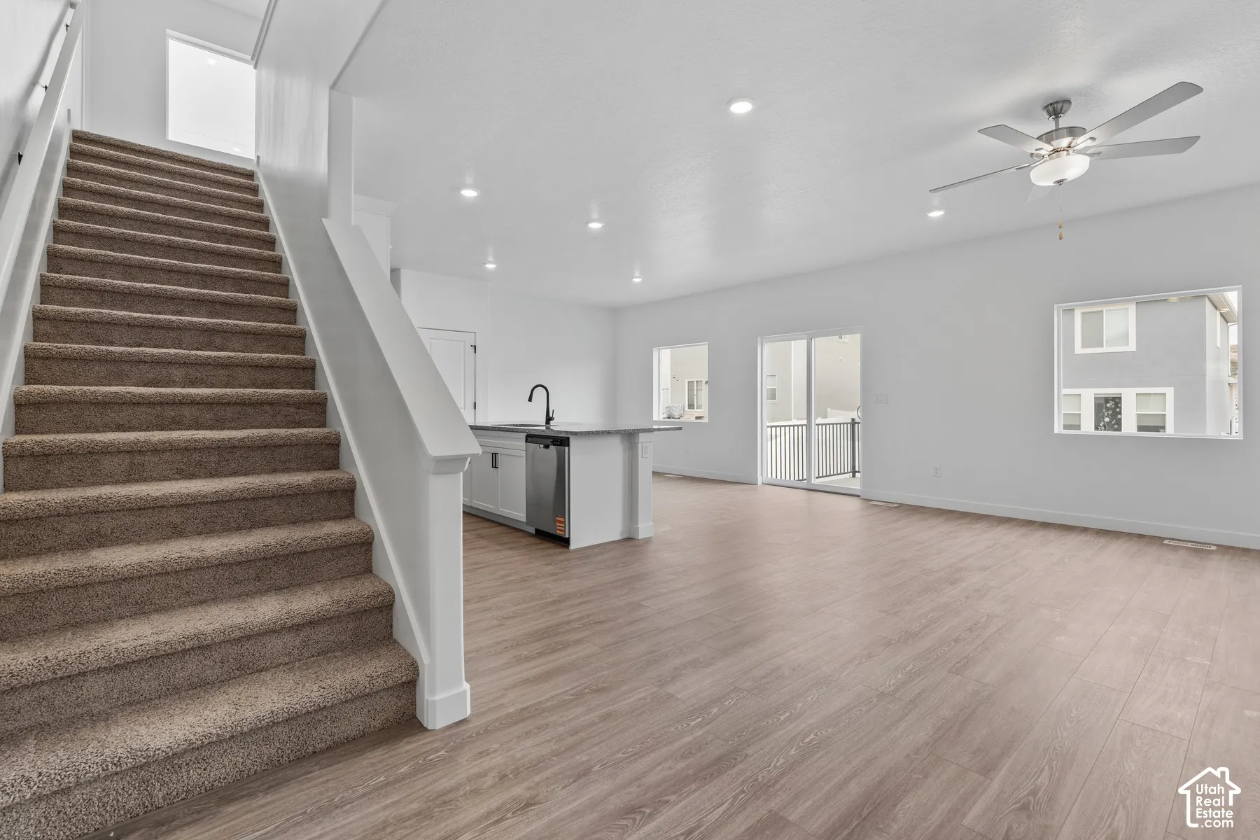 Carpeted staircase with white railing, wood-finish flooring, recessed lighting, and a ceiling fan with integrated lighting