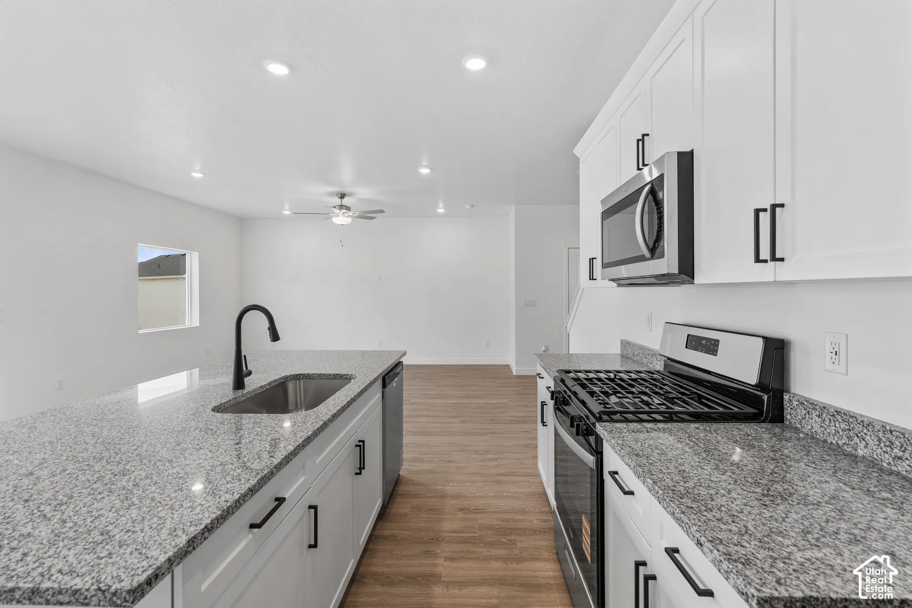 Kitchen featuring white cabinetry, a stainless steel gas range, microwave, and sink, and light-toned granite countertops