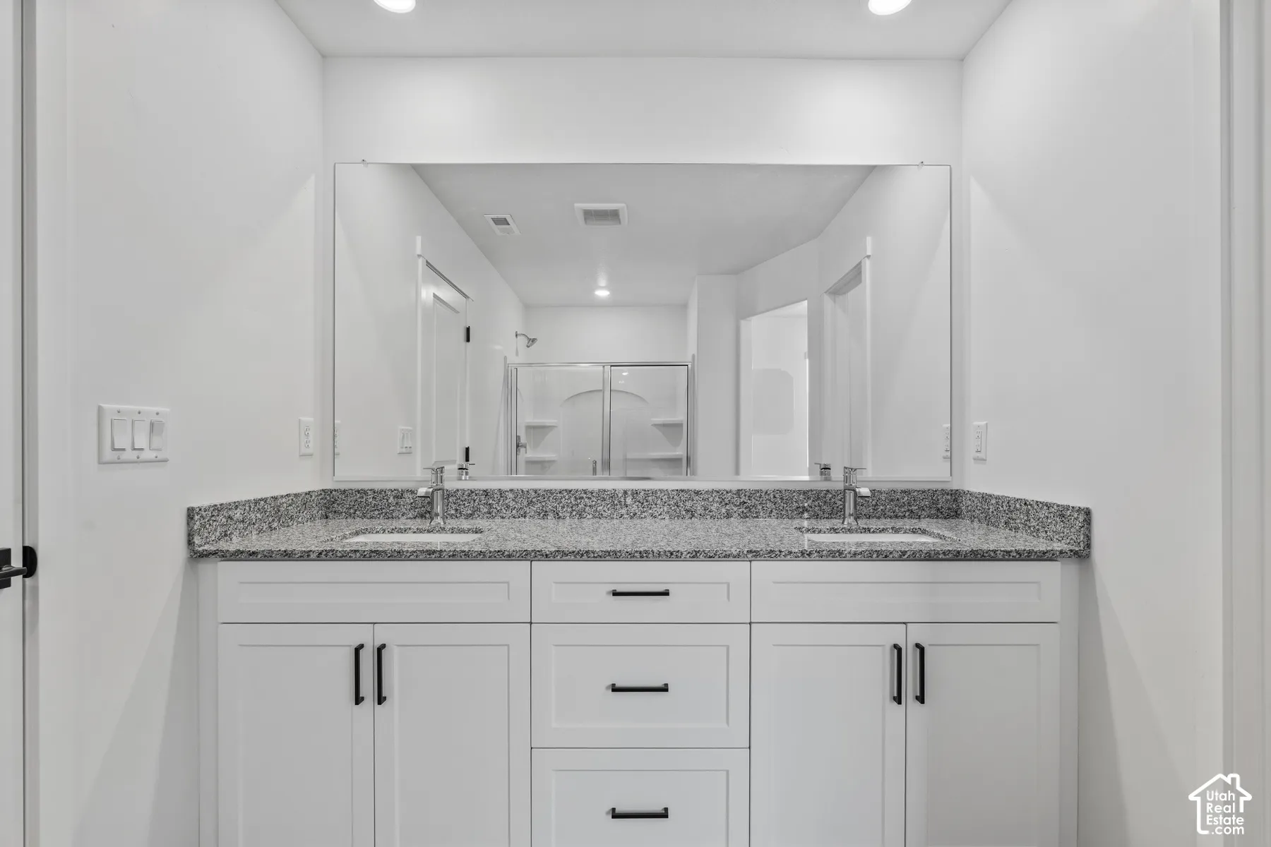 Dual vanity with a stone countertop, individual sinks, and white cabinetry
