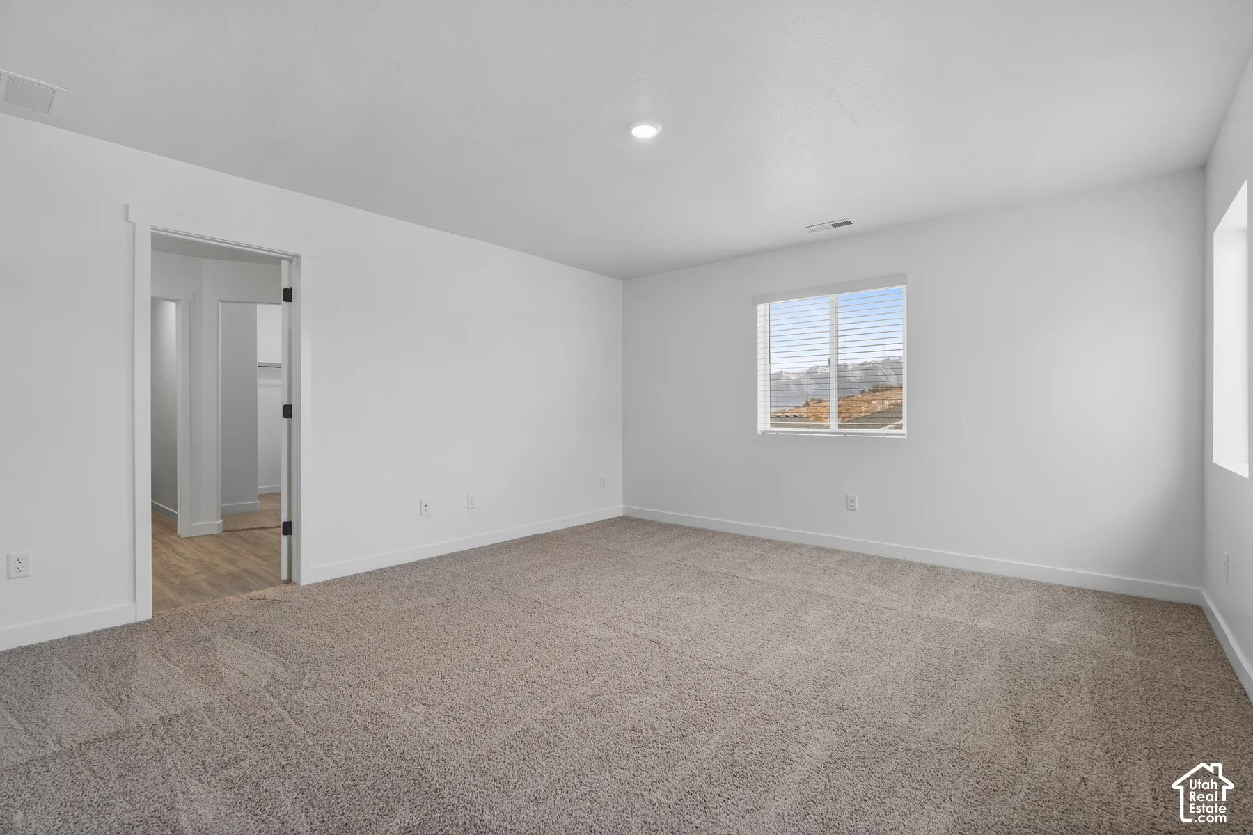 Wall-to-wall carpeting, recessed ceiling lighting, and a single window with horizontal blinds