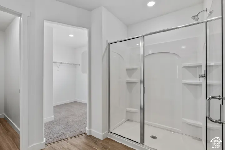 Glass-enclosed shower with built-in shelving, chrome fixtures, and wood-finish flooring