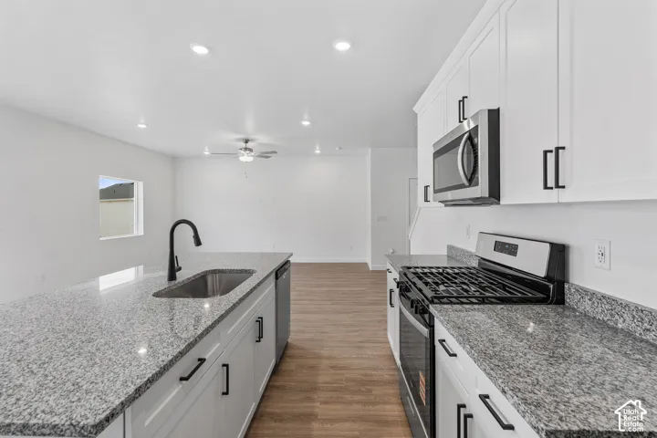 Kitchen featuring white cabinetry, a stainless steel gas range, microwave, and sink, and light-toned granite countertops