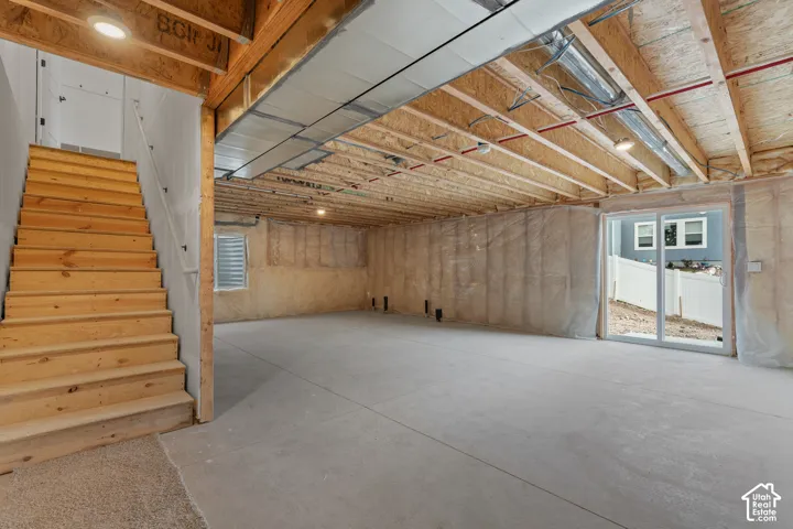 Unfinished basement space featuring a concrete floor, exposed wood ceiling joists, and a sliding glass door