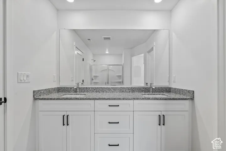 Dual vanity with a stone countertop, individual sinks, and white cabinetry