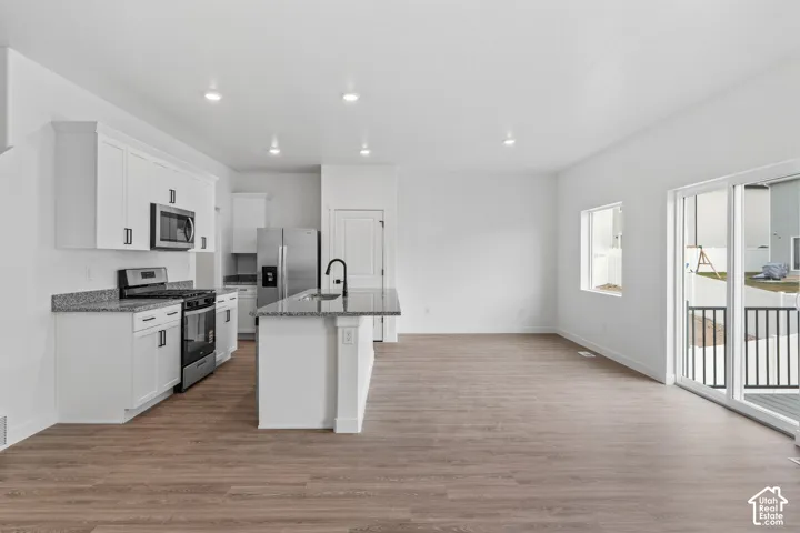 Open-concept living space featuring wood-finish flooring, white cabinetry, stainless steel appliances, and a kitchen island with a dark countertop