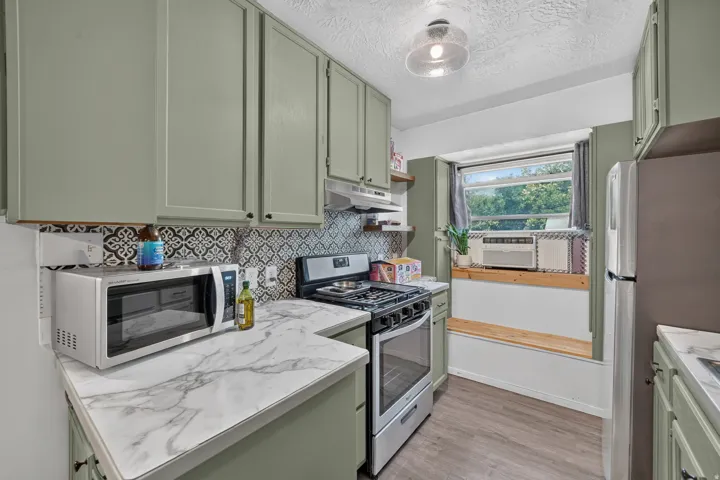 Kitchen featuring sage-green cabinetry, patterned tile backsplash, wood-finish flooring, and a built-in window bench