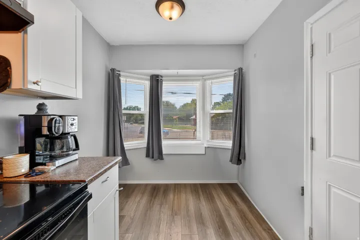 Bay window with blinds, wood-finish flooring, overhead lighting, white cabinetry, and a textured countertop