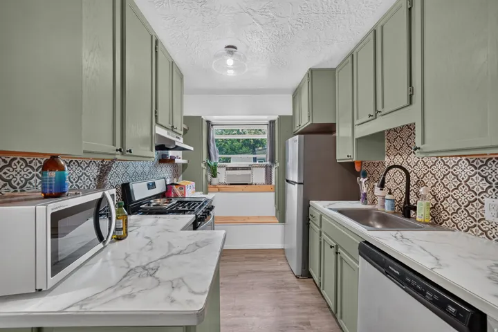 Galley kitchen featuring sage green cabinetry, patterned tile backsplash, wood-finish flooring, and white countertops