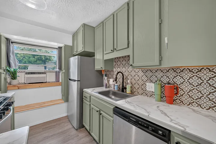 Kitchen with painted cabinetry, patterned backsplash, wood-finish flooring, and stainless steel appliances