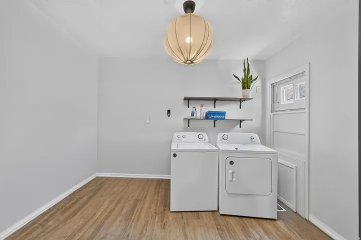 Laundry area featuring wood-finish flooring, white walls, and a contemporary ceiling light fixture
