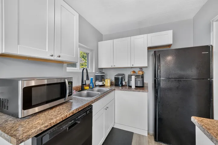 Kitchen featuring white cabinetry, wood-finish flooring, a double basin sink with a black faucet, and a built-in dishwasher