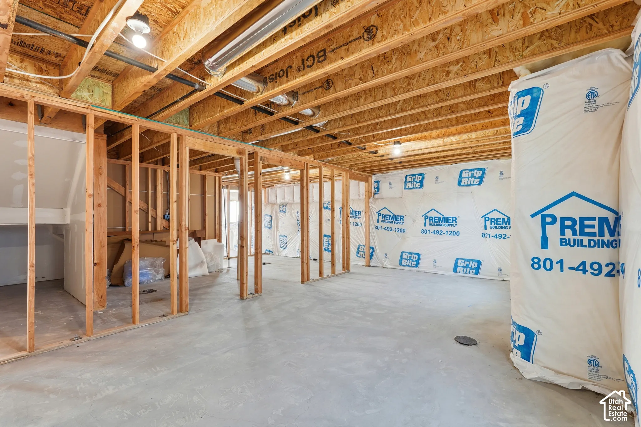 Unfinished basement with concrete flooring, wood framing, exposed joists, and wall insulation